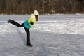 Girl skates on frozen forest lake on sunny frosty day. Makes swallow element