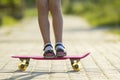 Girl slim legs in white socks and black sandals standing on pavement on plastic pink skateboard on bright sunny summer blurred bac