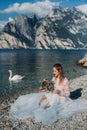 A girl in a smart white dress is sitting on the embankment of lake Garda.A woman is photographed against the background of a Royalty Free Stock Photo