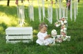 A girl in a smart white dress is sitting on the grass and looking at her hands soiled in cream.