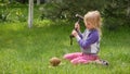 Girl smashes coconut with a heavy iron hammer sitting on the grass. 2 Royalty Free Stock Photo