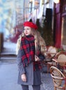 Girl with a smile in a gray coat and a red with long curls stands thoughtfully near a cafe on a background of a red facade Royalty Free Stock Photo