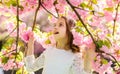 Girl on smiling face standing between sakura branches with flowers, defocused. Cute child enjoy nature on spring day