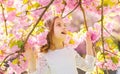 Girl on smiling face standing between sakura branches with flowers, defocused. Cute child enjoy nature on spring day