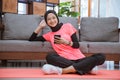 a girl in a smiling hijab gym clothes holding a cellphone while sitting relaxed on the floor