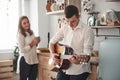 Girl is smiling. Young guitarist playing love song for his girlfriend in the kitchen Royalty Free Stock Photo