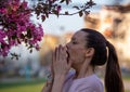 Girl sneezing in napkin in front of blooming tree in spring