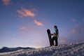 Girl snowboarder stands on a hillside against dark sunset sky Royalty Free Stock Photo