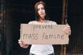 The girl is in soft focus, the focus is on cardboard inscription about the end of mass starvation