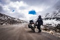 Girl solo ridder in ridding gears with loaded motorcycle at isolated road and snow cap mountains Royalty Free Stock Photo