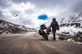 Girl solo ridder in ridding gears with loaded motorcycle at isolated road and snow cap mountains