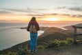 Girl solo traveler watching a beautiful sunset over the Pacific Ocean on top of a hill