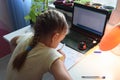 Girl solves math examples in notebook in front of laptop