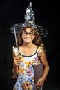 Girl sorceress, with a book and a magic wand, in a hat, on a black background