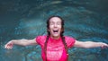 Girl in splashes of water with her mouth open and her eyes closed stands in a turquoise river