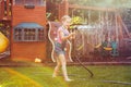 Girl splashing with gardening house on backyard on summer day
