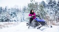 Girl on a sports snowmobile in a mountain forest. Athlete rides a snowmobile in the mountains. Snowmobile in snow Royalty Free Stock Photo