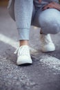 Girl squatted down to tie shoelaces on white sneakers on asphalt road, autumn sport concept outdoors