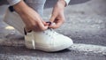 Girl squatted down to tie shoelaces on white sneakers on asphalt road, autumn sport concept outdoors