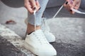 Girl squatted down to tie shoelaces on white sneakers on asphalt road, autumn sport concept outdoors