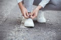 Girl squatted down to tie shoelaces on white sneakers on asphalt road, autumn sport concept outdoors