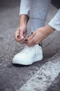 Girl squatted down to tie shoelaces on white sneakers on asphalt road, autumn sport concept outdoors