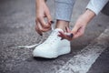 Girl squatted down to tie shoelaces on white sneakers on asphalt road, autumn sport concept outdoors