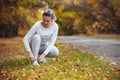 Girl squatted down to tie shoelaces on white sneakers on asphalt road, autumn sport concept outdoors