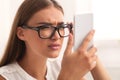 Girl Squinting Eyes Looking At Smartphone Through Eyeglasses Sitting Indoor Royalty Free Stock Photo