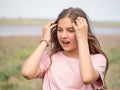 The girl squints. A teenage girl straightens her hair and covers her eyes from the bright light while standing in a spring meadow