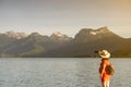 Girl with stalk hat and red dress on taking a selfie by a lake on a dock in front of big mountains Royalty Free Stock Photo