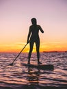 Girl stand up paddle boarding at dusk on a flat warm quiet sea with sunset colors Royalty Free Stock Photo