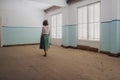 Girl standing in an abandoned empty house with big windows and fallen leaves