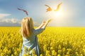 A girl standing in a bright yellow field with her hands reaching out to the sun and birds Royalty Free Stock Photo