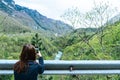 A Girl Standing on the Cliff and Taking Photograph of the Valley with the River. Red head making picture with smart phone to Tara