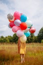 A girl standing in a field hiding her face behind balloons Royalty Free Stock Photo