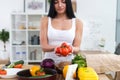 Girl standing at kitchen holding red tomato bunch in her hands. Housewife taking fresh ingredients for vegetable salad.