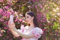 girl is standing near a pink blooming apple tree with smartphone Royalty Free Stock Photo