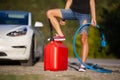 Girl standing next to an electric car. Holding charging cable and gassoline canister Royalty Free Stock Photo