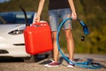 Girl standing next to an electric car. Holding charging cable and gassoline canister Royalty Free Stock Photo