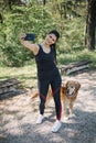 Girl standing in park with her dog taking selfie with phone Royalty Free Stock Photo