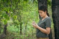 The girl is standing, taking notes in a small note book in the green forest