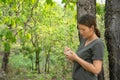 The girl is standing, taking notes in a small note book in the green forest