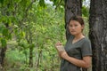 The girl is standing, taking notes in a small note book in the green forest