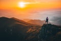 Girl standing on the top of the hill on the mountains meadow with beautiful colorful sunset over landscape