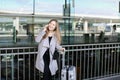 Girl standing with valise and talking by smartpone near airport. Royalty Free Stock Photo