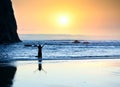 Girl standing in waves, arms raised to sky at sunset