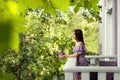 A girl stands on the balcony of her house. She is holding a mug of tea in her hands. Season of the year is summer. Royalty Free Stock Photo