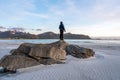 Girl stands on big rock on Ramberg beach in Lofoten island in Norway during sunset.