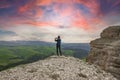 A girl stands on the edge of a cliff and takes pictures of a beautiful view.